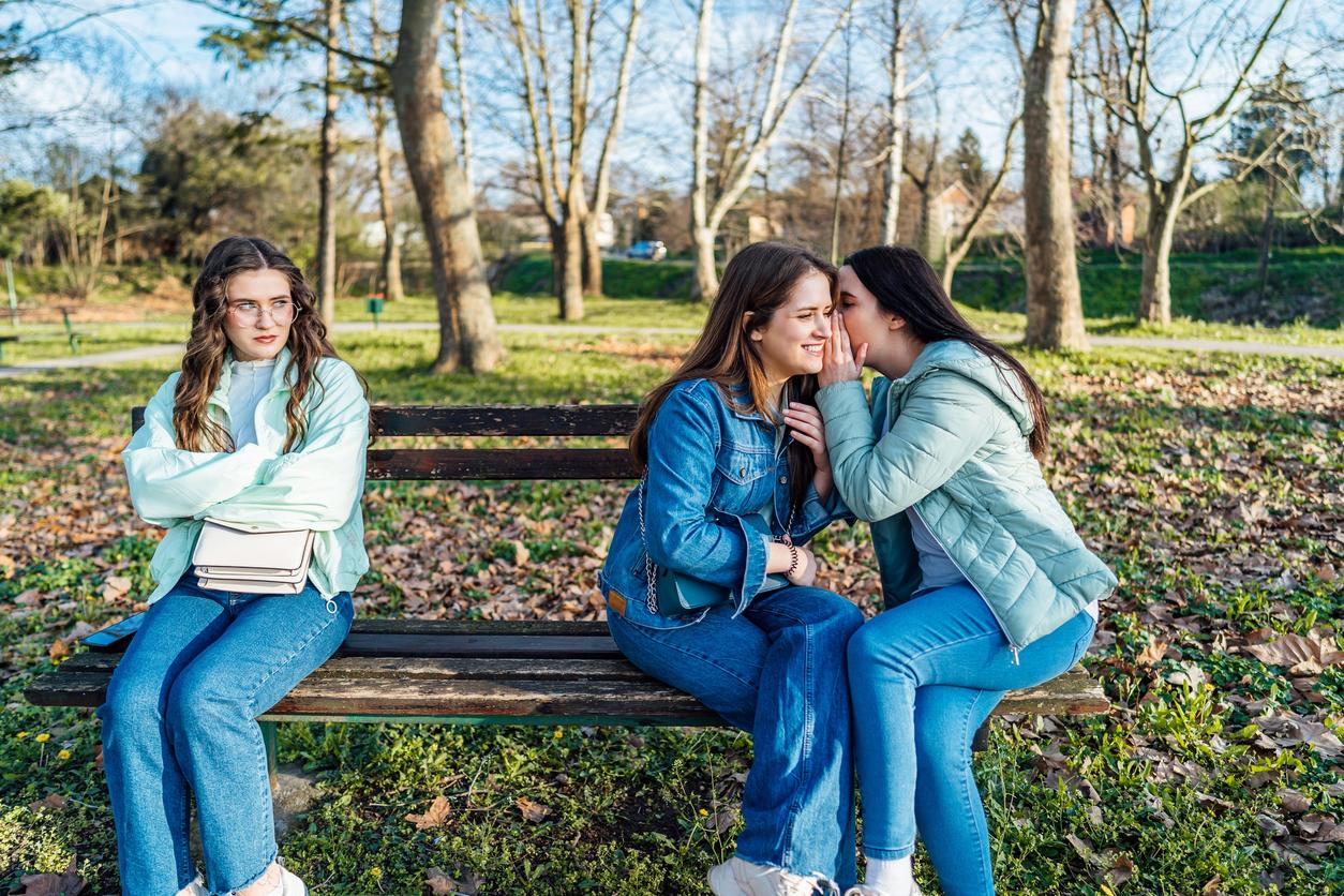 Mujer susurrando a otra frente a una chica molesta