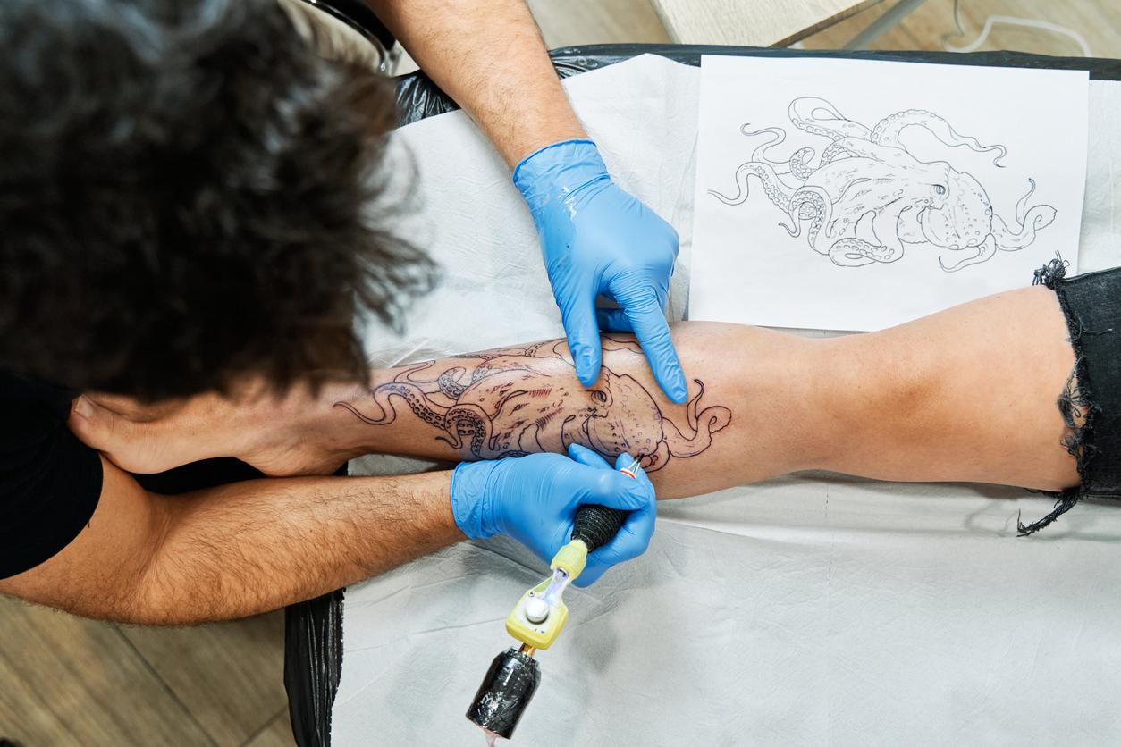 Tatuador dibujando un pulpo en la pierna de un cliente