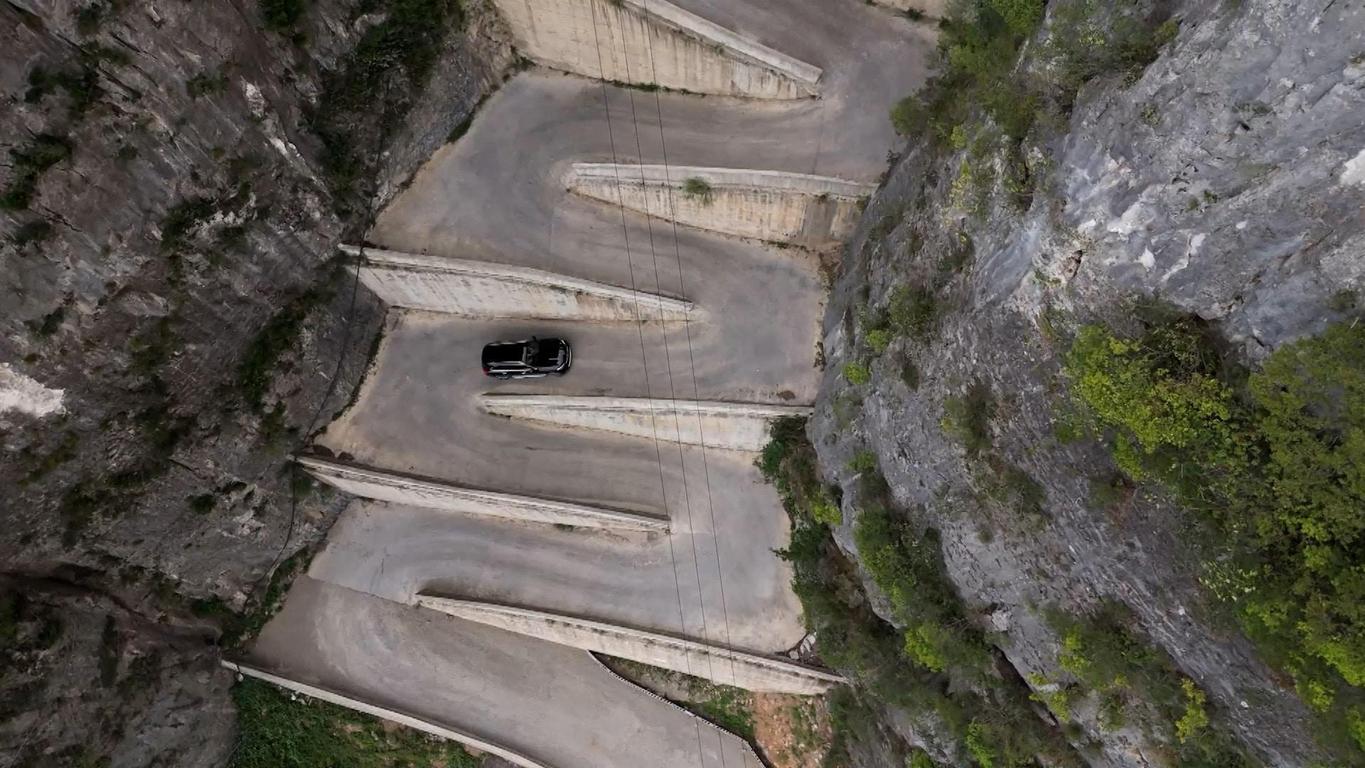 Vista aérea de la extrema carretera en zigzag de Lingpaishi en China con una ladera empinada y un coche descendiendo