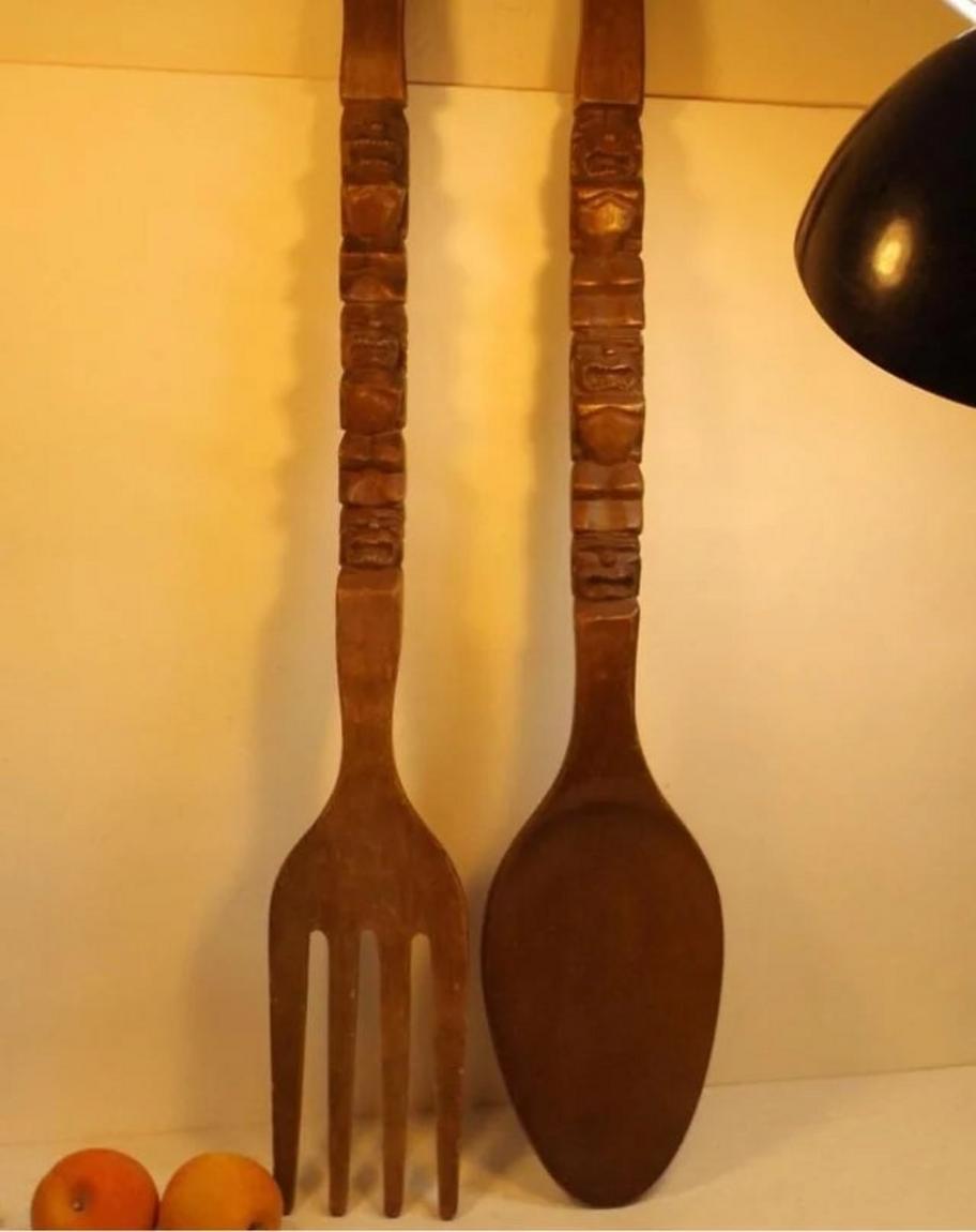 Tenedor y cuchara de madera gigantes colgados en la pared