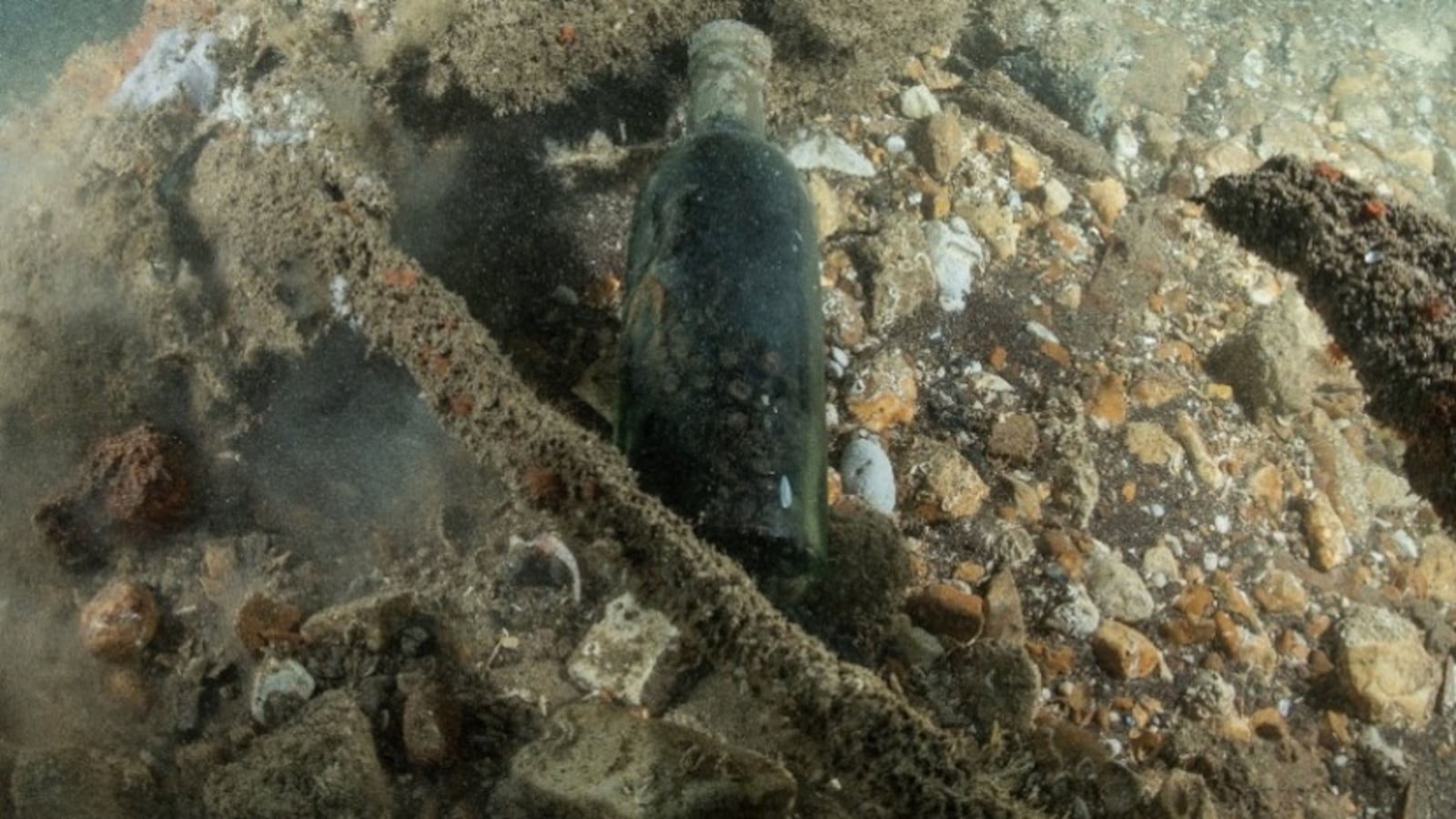 Botella de vidrio oscuro intacta y de pie sobre el fondo marino, entre piedras y restos del naufragio del Mindora