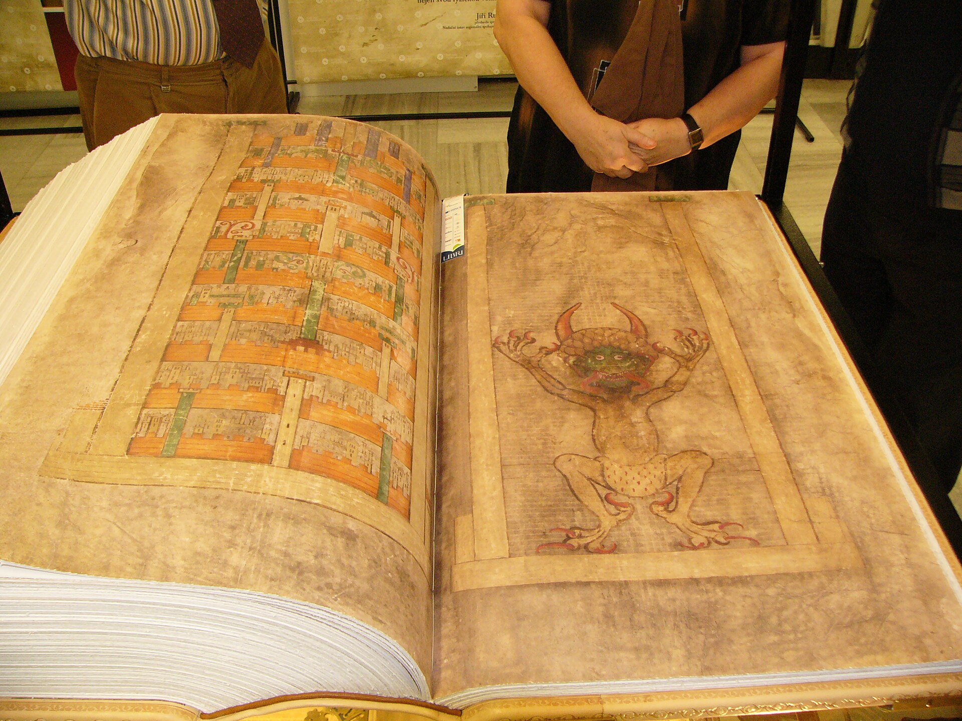 Facsímil a tamaño real del Codex Gigas abierto, con el retrato del diablo en la página derecha y personas detrás
