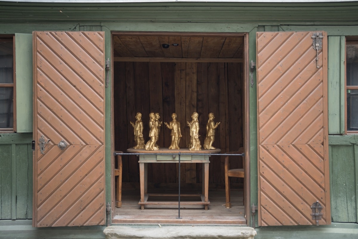 Seis estatuillas doradas de Mozart sobre una mesa de madera dentro de la caseta verde de La flauta mágica