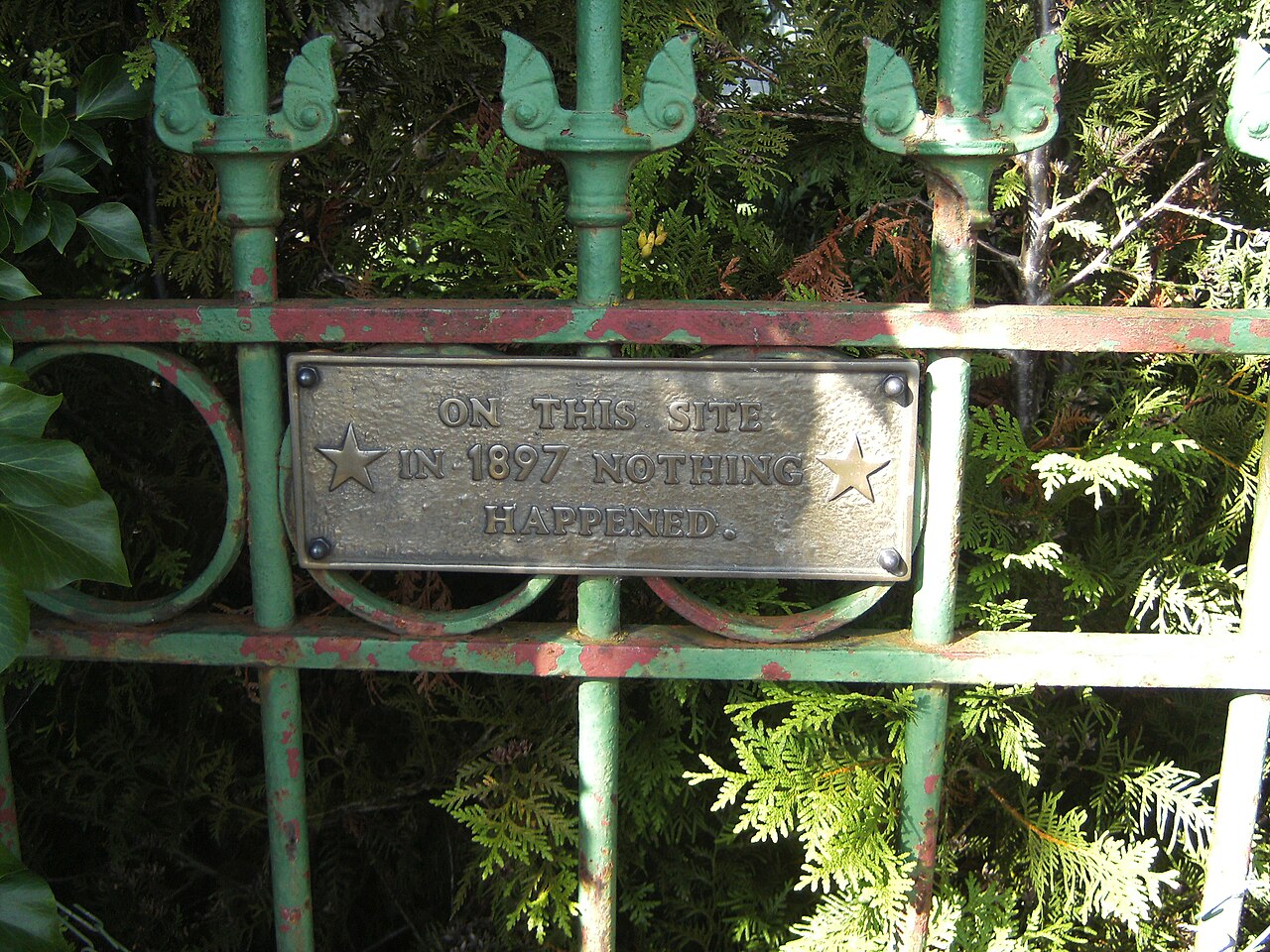 Placa metálica atornillada a una verja de hierro con el texto ON THIS SITE IN 1897 NOTHING HAPPENED entre dos estrellas grabadas