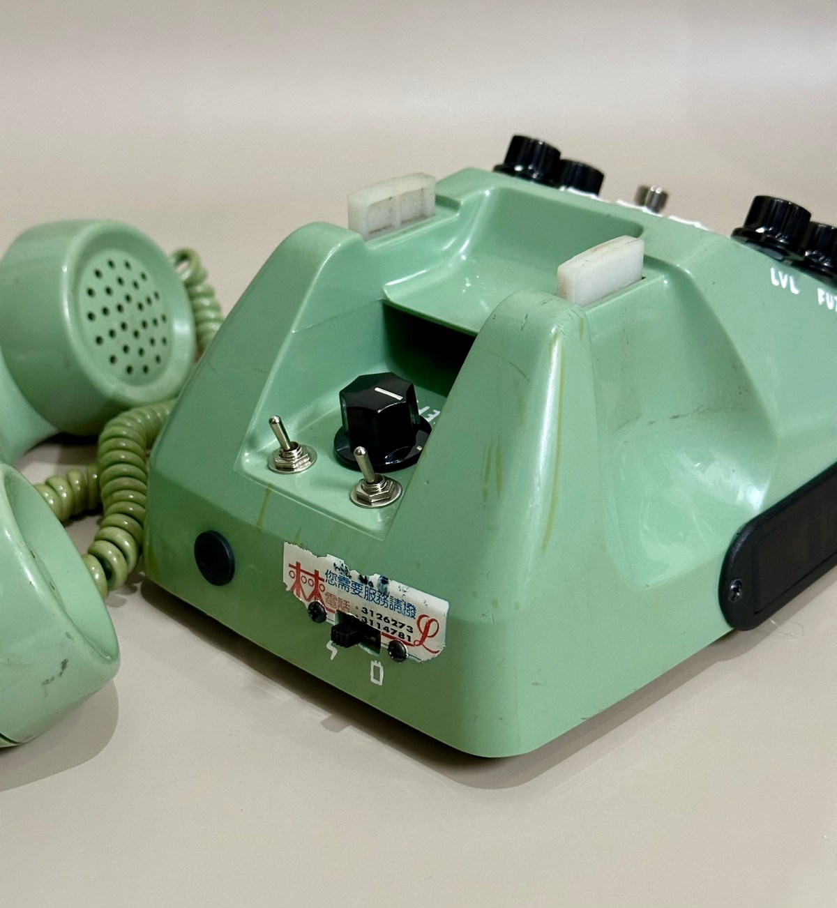 Teléfono verde menta convertido en pedal de fuzz, con dos interruptores, mandos rotulados LVL y FUZ y el auricular descolgado