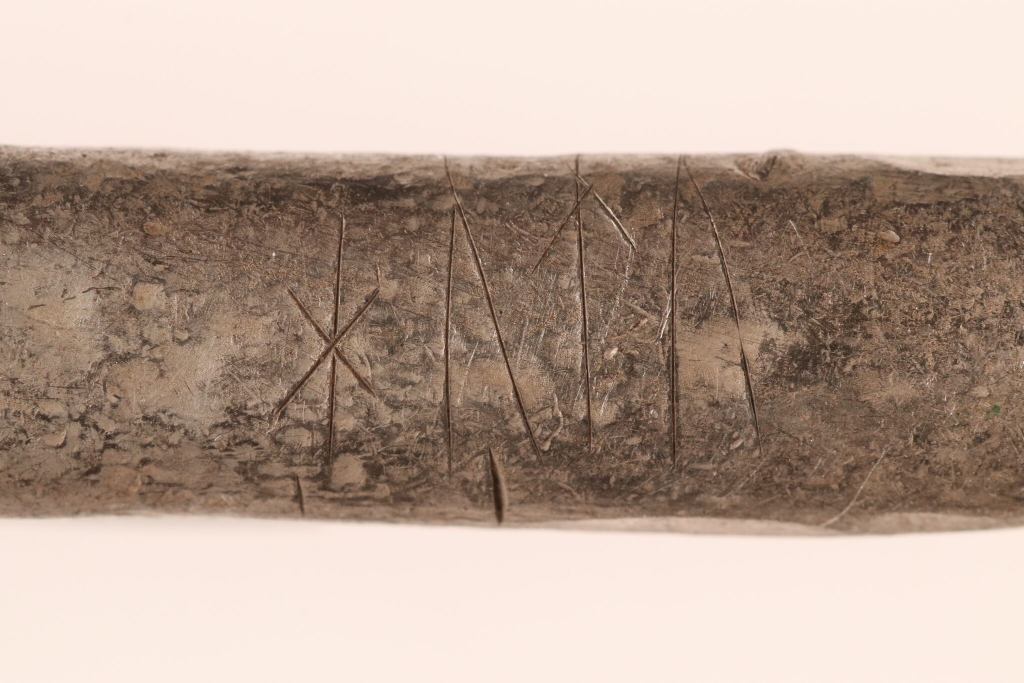 Barra alargada de plata vikinga con varias runas incisas, fotografiada sobre fondo claro de estudio