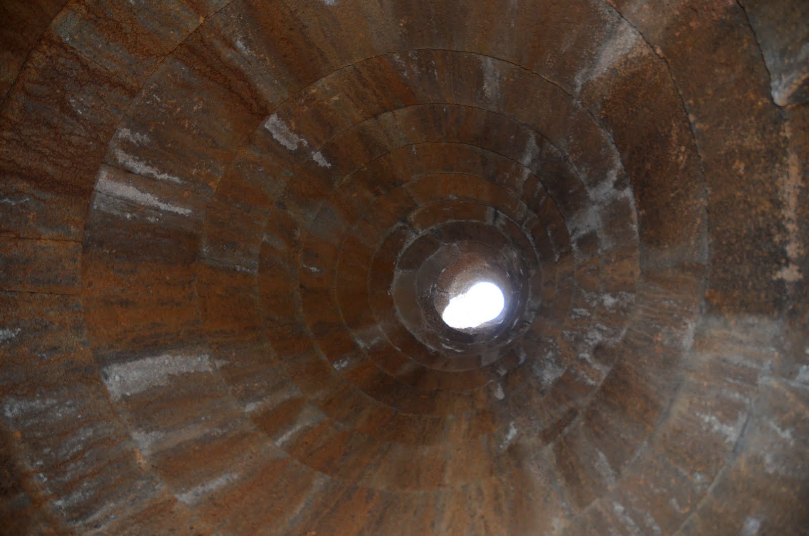 Bóveda de basalto en anillos concéntricos vista desde abajo, con un pequeño óculo circular de luz en el vértice