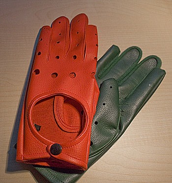 Par de guantes de conducir, uno rojo perforado y otro verde oscuro, superpuestos sobre una superficie de madera