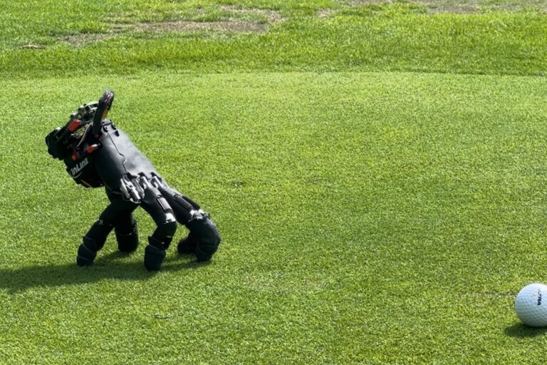 Mano robótica negra sin brazo apoyada sobre las puntas de sus dedos en el césped, junto a una pelota de golf