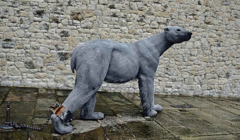 Escultura de malla de alambre de un oso polar encadenado por una pata, junto a un muro de piedra de la Torre de Londres