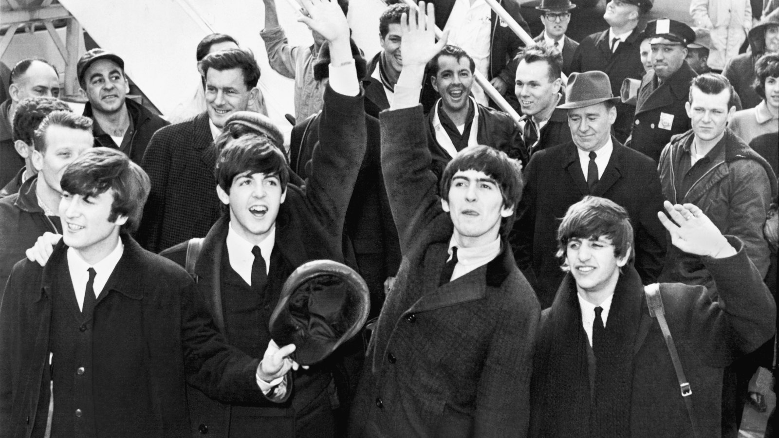 Los cuatro Beatles saludan con abrigos oscuros al bajar del avión en el aeropuerto Kennedy de Nueva York en febrero de 1964