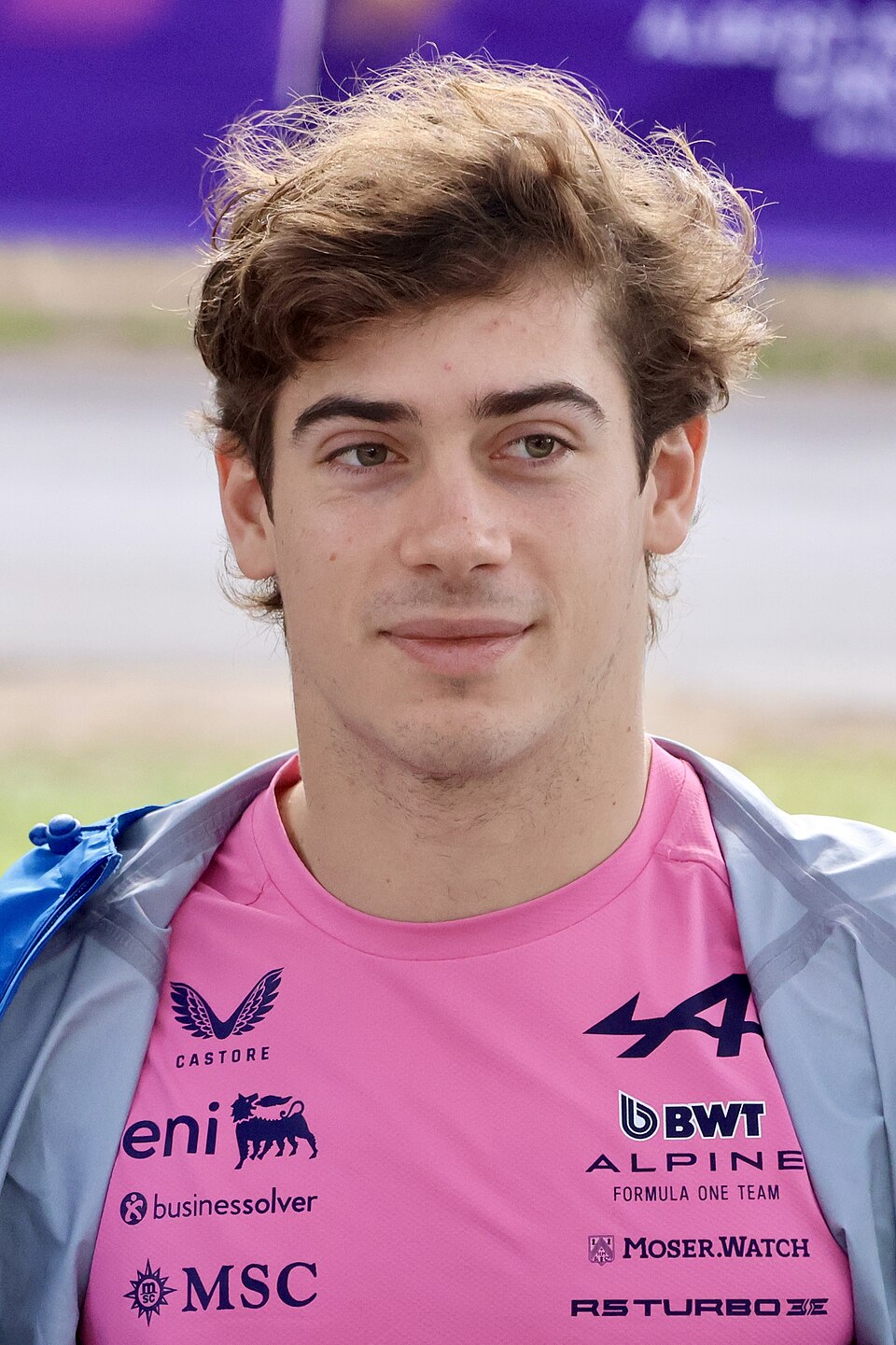Franco Colapinto con la camiseta rosa de Alpine y una chaqueta gris al hombro, sonriendo levemente en el paddock