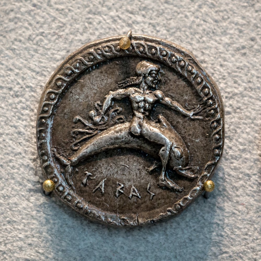 Moneda de plata de Taras con un joven desnudo a lomos de un delfín, rodeado por un borde decorativo