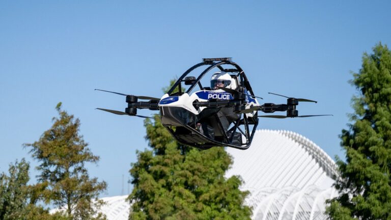 Dron tripulado blanco y negro con el rótulo POLICE y un piloto con casco volando sobre los árboles del campus de Florida Poly
