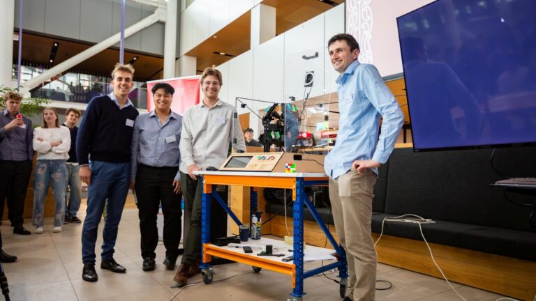 Cuatro estudiantes de la Universidad de Canterbury posan junto al robot que resuelve el cubo de Rubik 4x4 en menos de 10 segundos