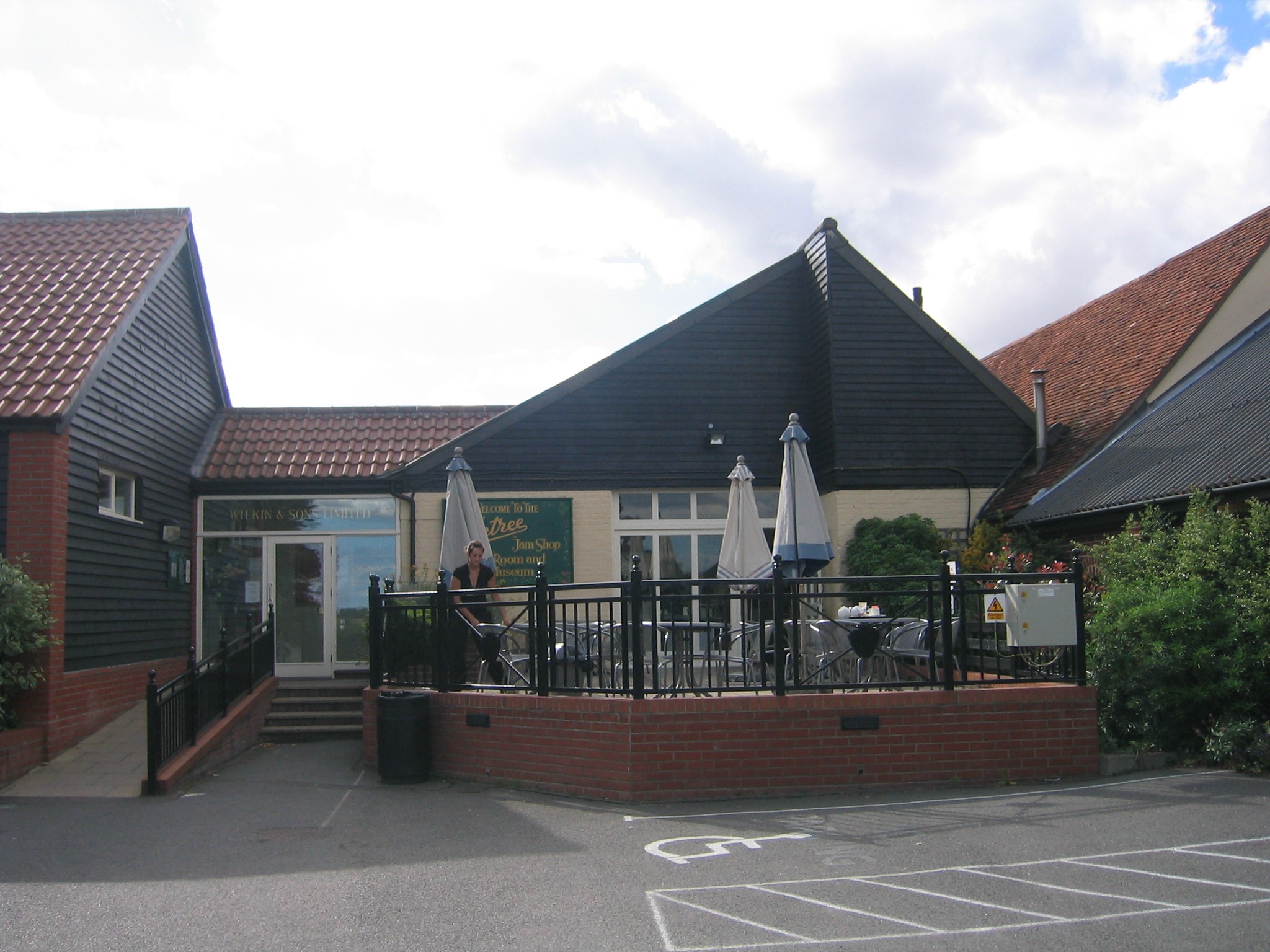 Edificio de ladrillo de la tienda, salón de té y museo de Wilkin & Sons en Tiptree, con terraza y sombrillas cerradas